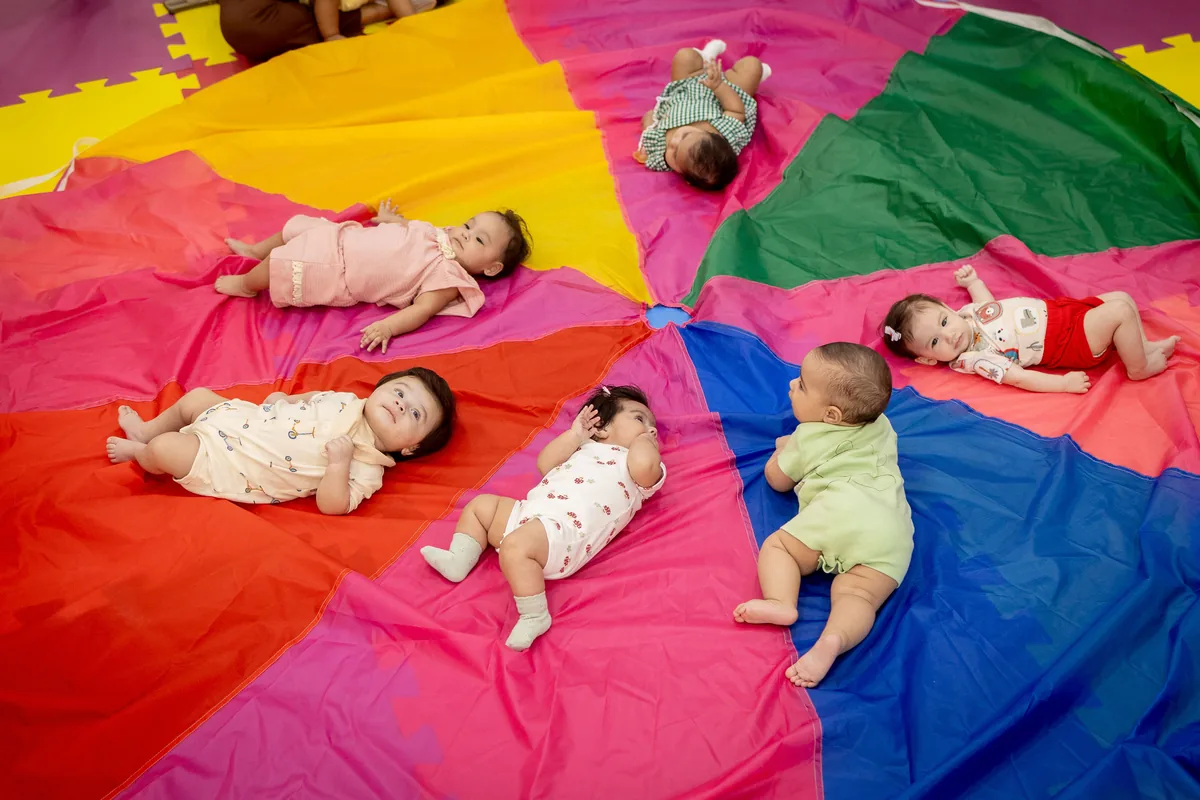 Bebês deitados sobre um paraquedas colorido durante uma atividade sensorial na Baby Gym Manaus