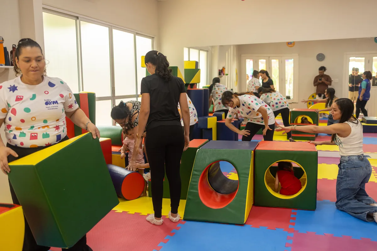Professoras e famílias brincando em um circuito de blocos e túneis de espuma sobre o tatame colorido da Baby Gym Manaus